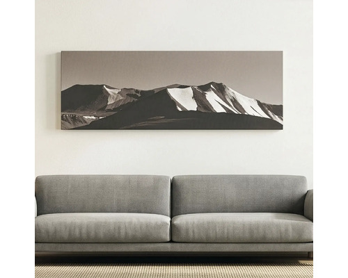 Tablou panoramic pe pânză cu peisaj montan înzăpezit deasupra unei canapele din material textil, decorațiune modernă într-o cameră luminoasă.
