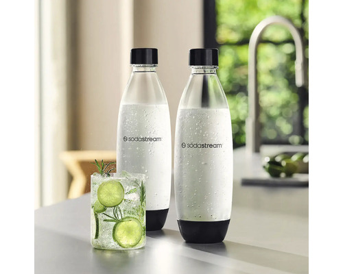 Două sticle din plastic SodaStream cu capac și bază negre lângă un pahar cu apă cu lămâie verde într-o bucătărie luminoasă.