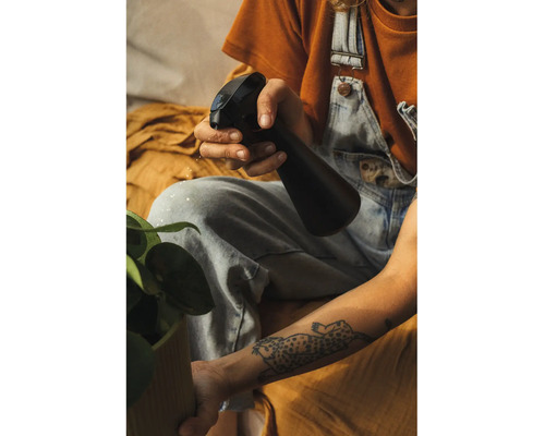 O persoană stropește o plantă de interior cu un pulverizator din plastic.