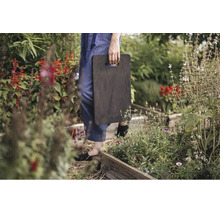 Protecție pentru genunchi Fiskars în grădină cu straturi din lemn și plante, purtată de o persoană.