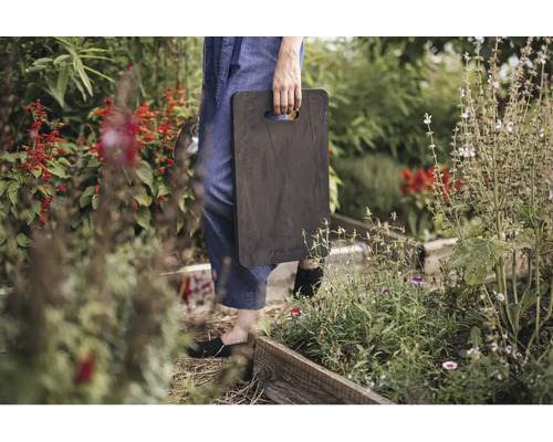 Protecție pentru genunchi Fiskars în grădină cu straturi din lemn și plante, purtată de o persoană.