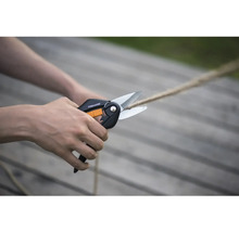 Foarfecă multifuncțională Fiskars tăind o frânghie pe o terasă din lemn luminoasă.
