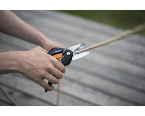 Foarfecă multifuncțională Fiskars tăind o frânghie pe o terasă din lemn luminoasă.