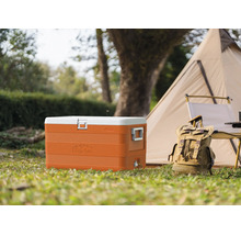 Geantă frigorifică portocalie mare cu capac alb pe iarbă lângă un cort și un rucsac într-un cadru de camping luminos.