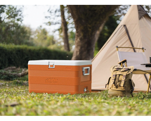 Geantă frigorifică portocalie mare cu capac alb pe iarbă lângă un cort și un rucsac într-un cadru de camping luminos.