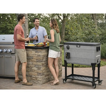 Trei persoane pe o terasă lângă o bucătărie de exterior din piatră cu grătar pe gaz și o ladă frigorifică mare, mobilă pe un suport cu roți.