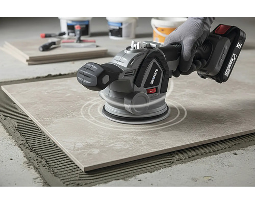 Vibrator pentru plăci ceramice cu Graphite Logo pe o placă de pardoseală într-o zonă de lucru luminoasă. Placa este pe un pat de adeziv.