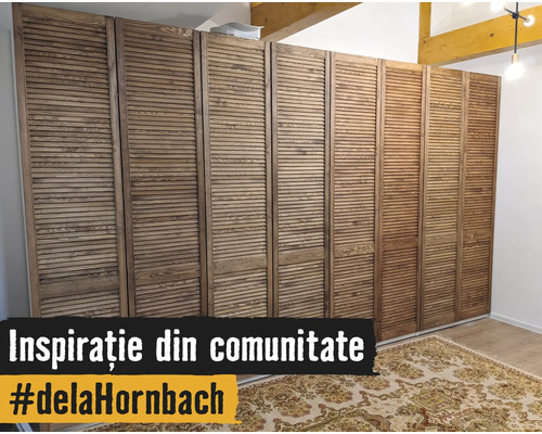 Dulap mare cu uși lamelare din lemn într-o cameră luminoasă, cu un covor cu model și grinzi de lemn pe tavan. Hornbach Logo.