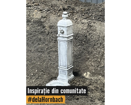 Cișmea decorativă de grădină cu aspect de piatră, robinet metalic și bazin pe pământ.