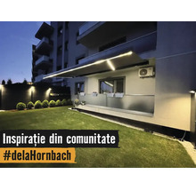 Copertină retractabilă iluminată cu benzi LED integrate deasupra unui balcon cu balustradă de sticlă și gazon îngrijit pe timp de noapte.
