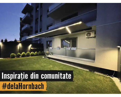 Copertină retractabilă iluminată cu benzi LED integrate deasupra unui balcon cu balustradă de sticlă și gazon îngrijit pe timp de noapte.