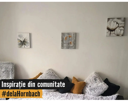 Decorațiune de perete cu trei tablouri pătrate cu motive cu fluturi și flori deasupra unei canapele cu perne pufoase și netede.