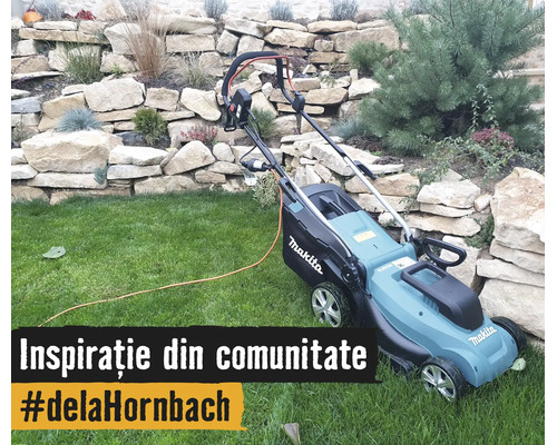 Mașină electrică de tuns gazonul Makita cu Makita Logo pe o peluză în fața unui zid de piatră cu plante în grădină.