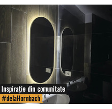 Oglindă de baie ovală modernă cu iluminare LED pe un perete cu aspect de lemn deasupra unui lavoar alb.