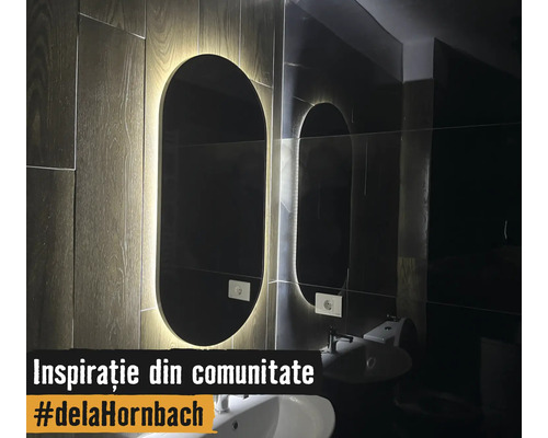 Oglindă de baie ovală modernă cu iluminare LED pe un perete cu aspect de lemn deasupra unui lavoar alb.