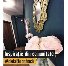 Oglindă decorativă rotundă de perete cu ramă aurie în formă de frunze lângă bujori roz într-o vază de sticlă într-un hol amenajat modern.
