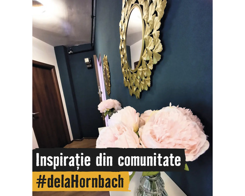 Oglindă decorativă rotundă de perete cu ramă aurie în formă de frunze lângă bujori roz într-o vază de sticlă într-un hol amenajat modern.