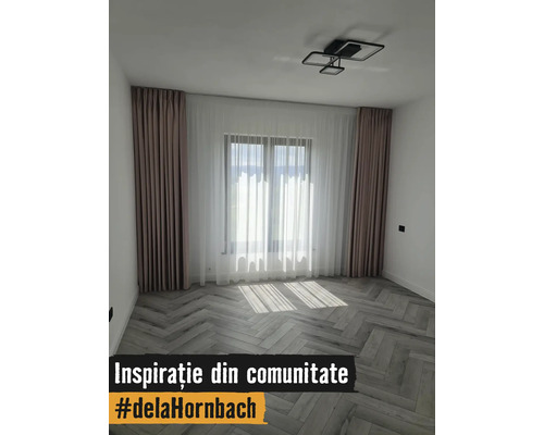 Cameră modernă cu pardoseală tip spic, perdele în culori deschise și plafonieră cu design geometric.
