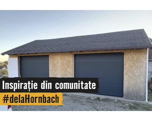 Garaj dublu în construcție cu pereți din plăci OSB, două uși secționale antracit și acoperiș din șindrilă bitumoasă.