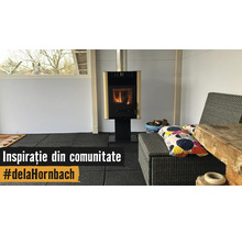 Șemineu modern pe o pardoseală neagră într-o cameră luminoasă cu mobilier de grădină din ratan și o masă din lemn rustic.
