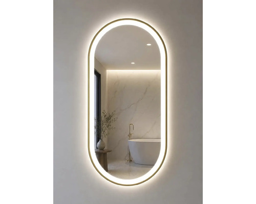 Oglindă de baie ovală cu cadru auriu și iluminare LED. Oglinda reflectă o baie luminoasă cu cadă de sine stătătoare și perete de marmură.