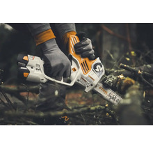 Persoană cu mănuși de lucru care taie o creangă cu un motoferăstrău cu acumulator Stihl în aer liber.