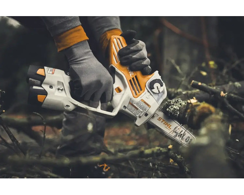 Persoană cu mănuși de lucru care taie o creangă cu un motoferăstrău cu acumulator Stihl în aer liber.
