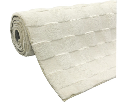 Covor plușat moale, de culoare crem, cu model în relief cu pătrate, parțial desfășurat.