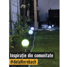 Mai multe lămpi solare de grădină în formă de sfere de-a lungul marginii unui gazon, noaptea. Sferele luminează în diverse culori.