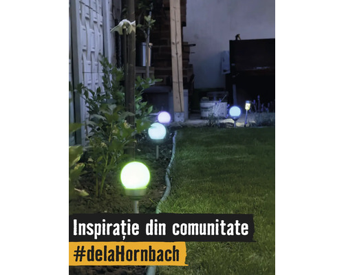 Mai multe lămpi solare de grădină în formă de sfere de-a lungul marginii unui gazon, noaptea. Sferele luminează în diverse culori.