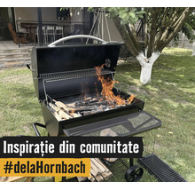 Grătar metalic cu cărbuni deschis, cu lemne aprinse în grădină. Dotat cu raft pentru menținerea căldurii, raft lateral și roți.