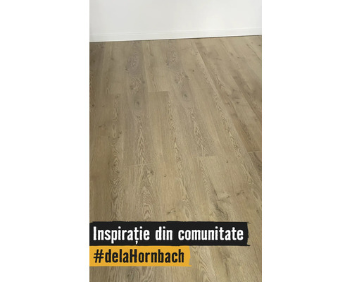 Pardoseală laminată cu aspect de lemn, nervuri naturale și plăci late, montată cu plintă.