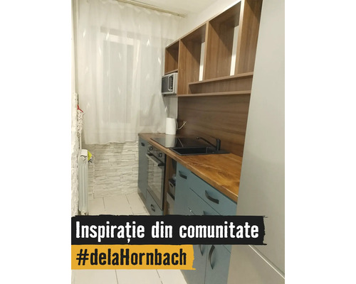 Bucătărie modernă și compactă cu dulapuri albastru deschis, blat de lucru din lemn, chiuvetă neagră, plită vitroceramică și cuptor încorporabil.