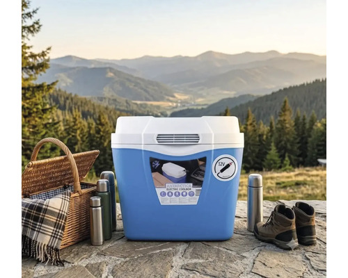 Ladă frigorifică electrică cu conexiune de 12 Volți pentru camping, lângă coș de picnic, termosuri și bocanci de munte în fața unui peisaj montan.