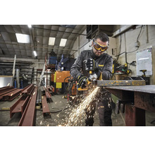 Un muncitor cu ochelari și mănuși de protecție taie metal cu un polizor unghiular într-un atelier, generând scântei.