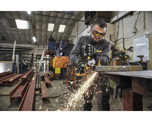 Un muncitor cu ochelari și mănuși de protecție taie metal cu un polizor unghiular într-un atelier, generând scântei.