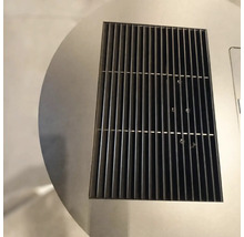 Vedere de aproape a unei grile de ventilație dreptunghiulare din metal negru, integrată într-o suprafață circulară din oțel inoxidabil.