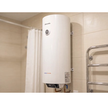 Boiler electric vertical Fornello Aquacalda într-o baie placată cu gresie lângă o perdea de duș și un radiator pentru prosoape.