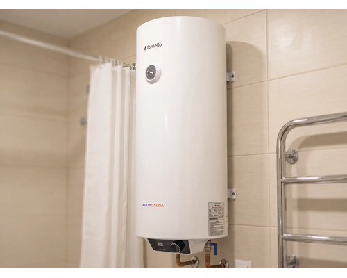 Boiler electric vertical Fornello Aquacalda într-o baie placată cu gresie lângă o perdea de duș și un radiator pentru prosoape.