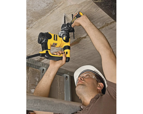 Un muncitor găurește un tavan de beton cu un ciocan rotopercutor DeWalt, purtând cască de protecție și ochelari.