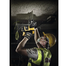Muncitor cu cască de protecție, mască de praf și ochelari găurește cu un rotopercutor DeWalt tavanul de beton.