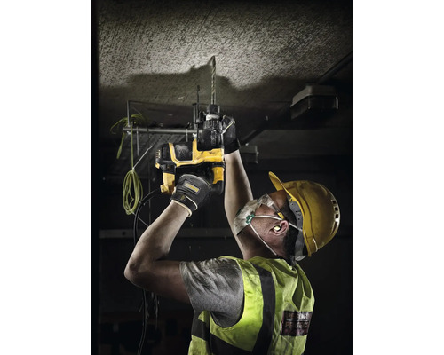 Muncitor cu cască de protecție, mască de praf și ochelari găurește cu un rotopercutor DeWalt tavanul de beton.