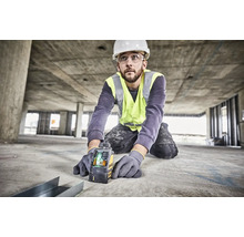 Meșter cu cască de protecție și vestă reflectorizantă folosind un laser în cruce Dewalt pe un șantier de beton pentru aliniere precisă.