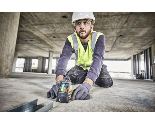 Meșter cu cască de protecție și vestă reflectorizantă folosind un laser în cruce Dewalt pe un șantier de beton pentru aliniere precisă.