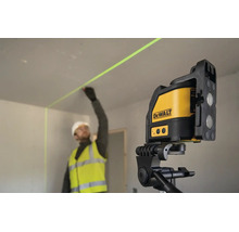 Un muncitor în construcții echipat de lucru marchează un perete folosind un laser cu linii în cruce DeWalt pe un trepied în interior.