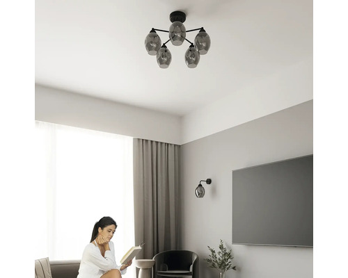 Plafoniera modernă cu cinci abajururi din sticlă fumurie într-un living luminos cu o femeie care citește