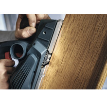 O rindea electrică este ghidată manual pentru a netezi marginea unei scânduri de lemn.