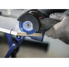 Un dispozitiv de tăiere multifuncțional cu acumulator Bosch care taie o placă de lemn cu un disc de tăiere, manevrat cu o mână înmănușată.