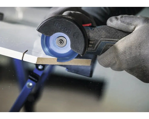 Un dispozitiv de tăiere multifuncțional cu acumulator Bosch care taie o placă de lemn cu un disc de tăiere, manevrat cu o mână înmănușată.
