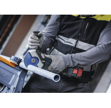 Meșter care taie o țeavă cu un polizor unghiular cu acumulator Bosch purtând mănuși de protecție